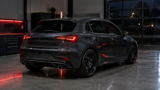 Hatchback compatta grigio scuro vista di tre quarti posteriore in officina, con spoiler e calotte in fibra di carbonio