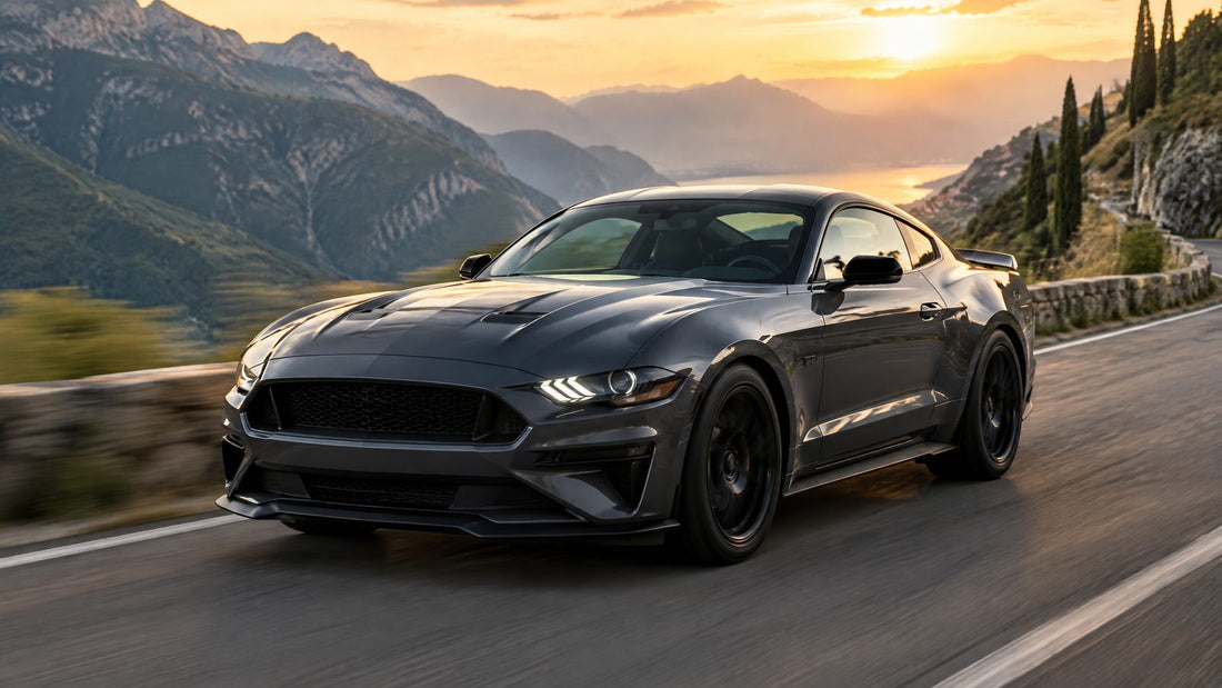 Ford Mustang grigio scuro con dettagli neri su una strada di montagna al tramonto, vista anteriore di tre quarti