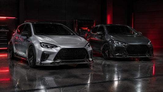 Due hatchback compatte, argento e grigio scuro, con splitter e calotte in carbonio in un garage buio con luci rosse